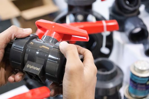 Close-up of hands examining a Hydroplast industrial valve at a trade expo.
